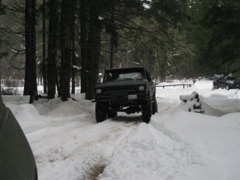 1979 Ford Bronco - A lifted 1979 Ford Bronco navigates a snowy forest road, with another vehicle visible in the background.