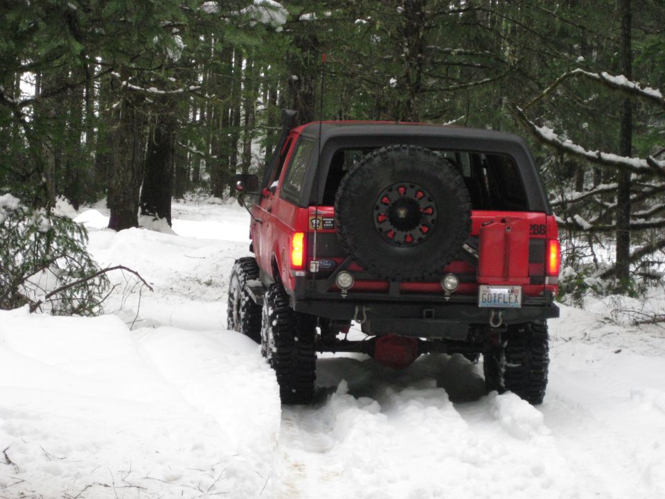 Red 1979 Ford Bronco with spare tire on back driving on snowy trail