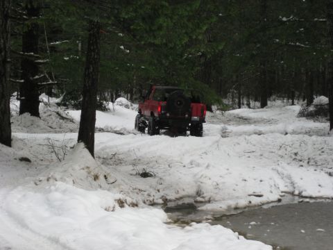 1979 Ford Bronco - A red SUV navigates a snowy forest road, its lifted suspension and large tires suited for the terrain.