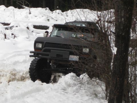 1979 Ford Bronco - A black 1979 Ford Bronco navigates a snowy trail, its large tires digging into the snow.