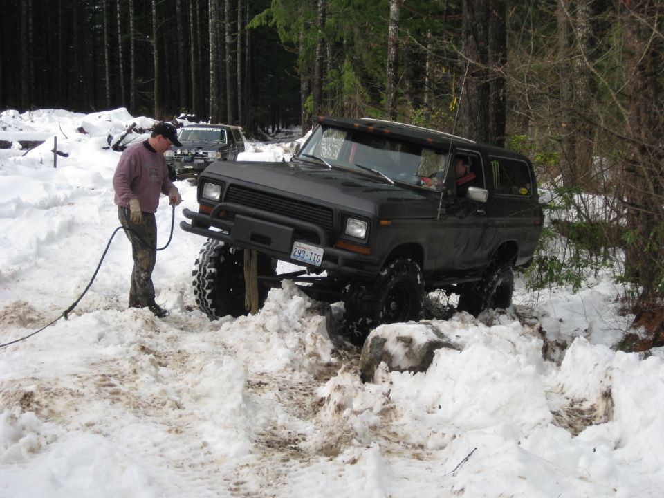 guy with hose near lifted Bronco stuck in snow, another SUV behind it
