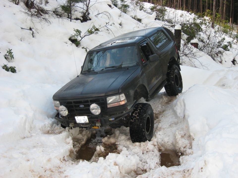 Dark SUV with lifted suspension and off-road tires driving through deep snow on a wooded trail