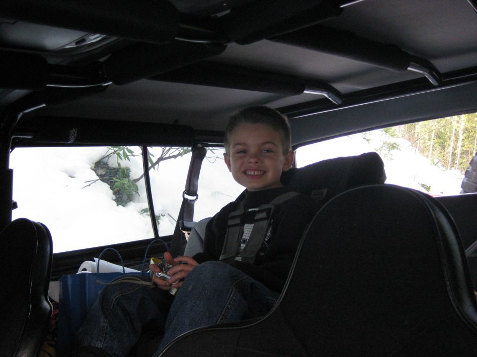 Kid in the back seat of a vehicle, looking out at a snowy landscape