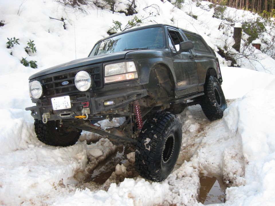 Modified Ford Bronco with large tires driving through snow, front bumper and winch visible