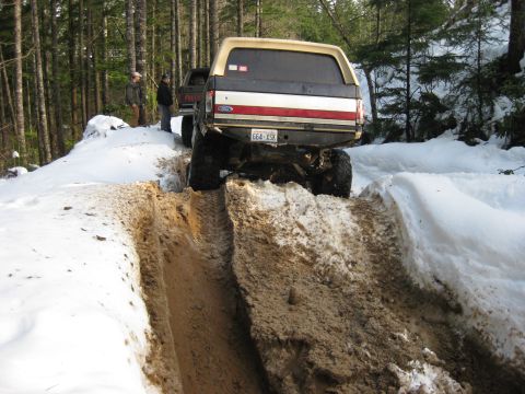 1979 Ford Bronco - A tan and brown Ford Bronco navigates a muddy and snowy trail with another vehicle behind it.