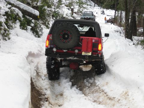 1979 Ford Bronco - Off-road Bronco navigates a snow-covered path with other vehicles and people in the distance.