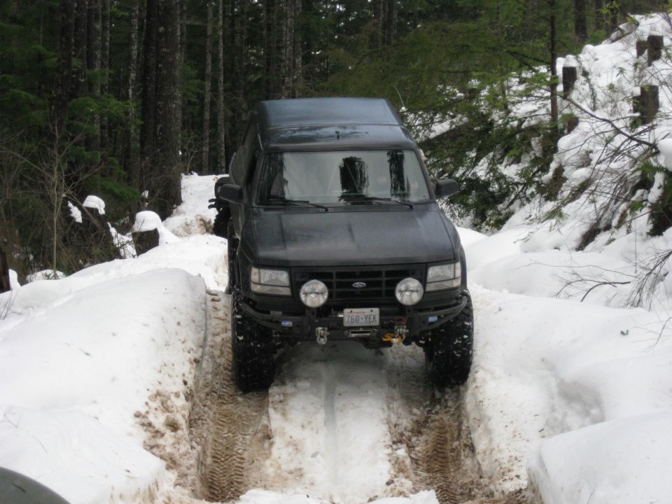 Dark SUV with aftermarket bumper and lights driving through snow