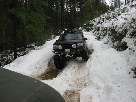 1979 Ford Bronco - A black Ford Bronco navigates a snow-covered trail in a wooded area, with another vehicle partially visible in the foreground.