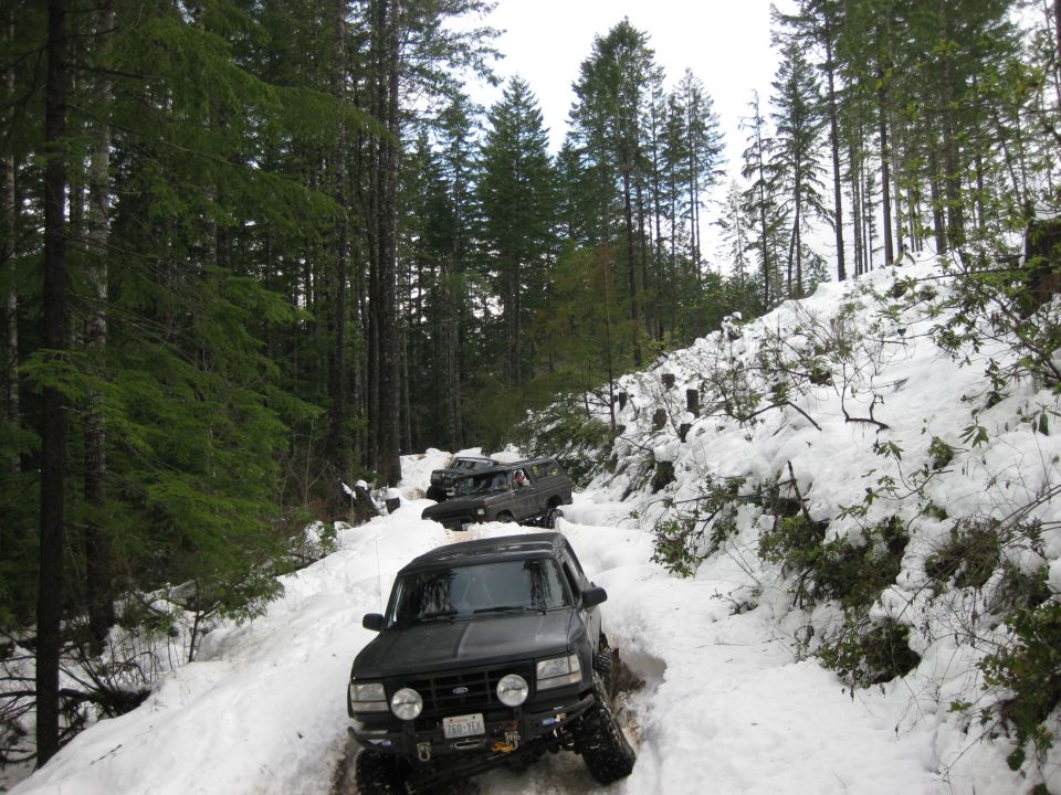 Black Ford Bronco driving on a snowy forest road, front view