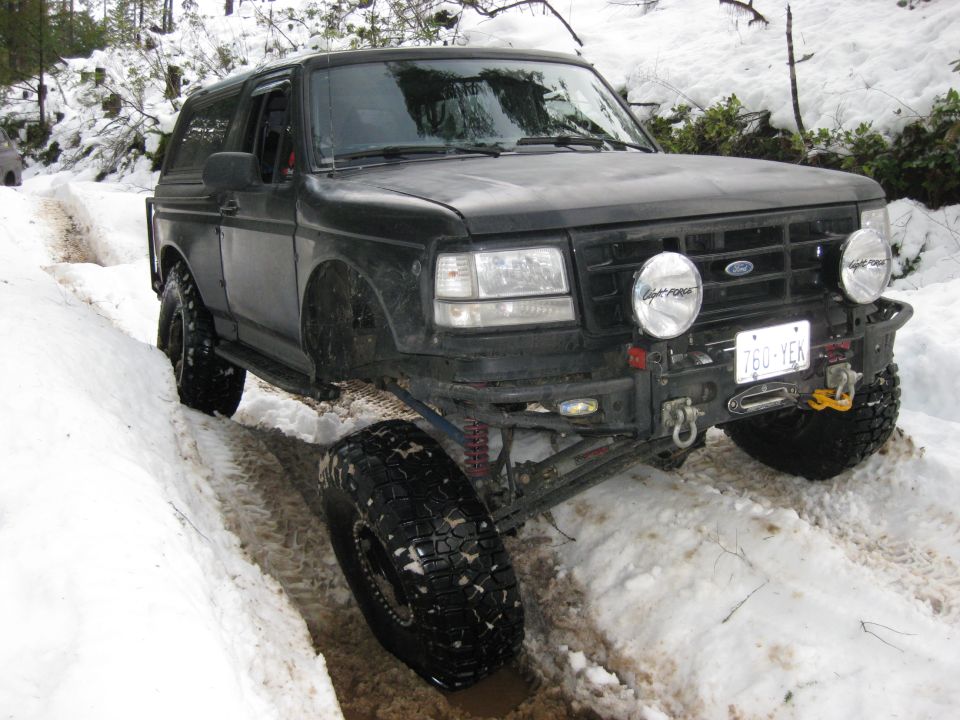Black Ford Bronco with off-road tires driving in snow, front bumper has lights and winch. License plate 760-YEN