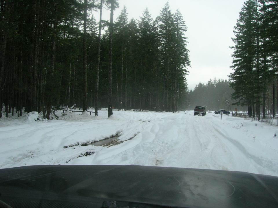 Red 1996 Ford Bronco driving on a snow-covered road through a forest