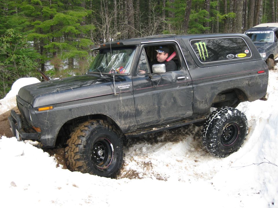 Black Ford Bronco with monster energy sticker stuck in snow, another vehicle behind it
