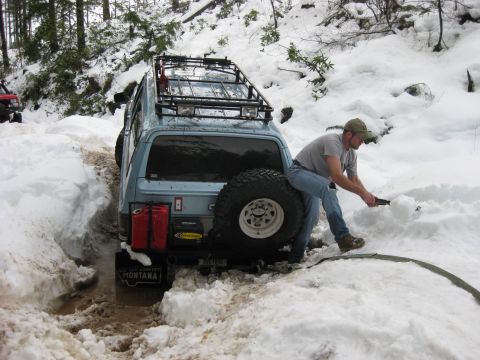 1979 Ford Bronco - A light blue 1979 Ford Bronco is stuck in the snow while a man attempts to dig it out.
