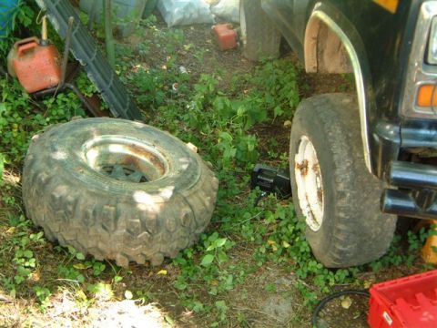 1982 Ford Bronco - A spare tire lies on the ground next to the front wheel well of a black SUV.