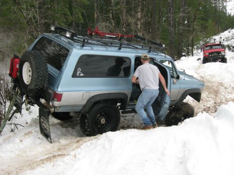1979 Ford Bronco - A blue SUV navigates a snowy trail with a man exiting the vehicle.