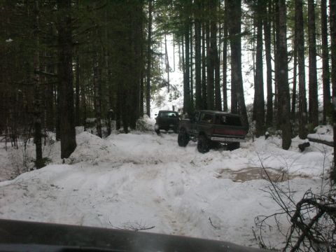 1996 Ford Bronco - Two off-road vehicles navigate a snow-covered path through a dense forest.