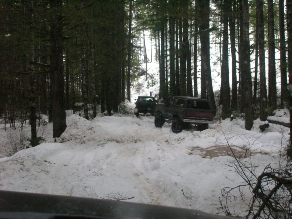 Dark brown Ford Bronco with lifted suspension driving on a snowy forest road