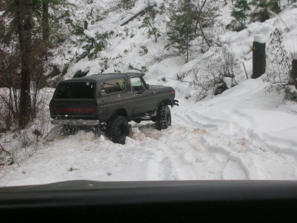 Dark gray Ford Bronco with lifted suspension and large tires driving in snow