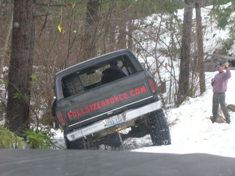 Ford Bronco stuck in snow with 'fullsizebronco.com' on the back. Another person stands nearby