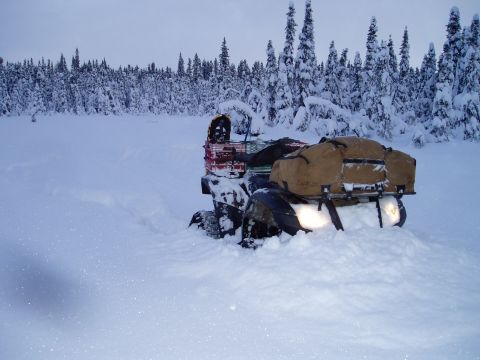 2000 Ford E350 - An ATV is partially buried in snow, with a forest of snow-covered trees behind it.