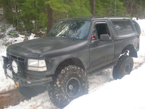 1996 Ford Bronco - A black 1996 Ford Bronco navigates a snowy trail with its large tires.