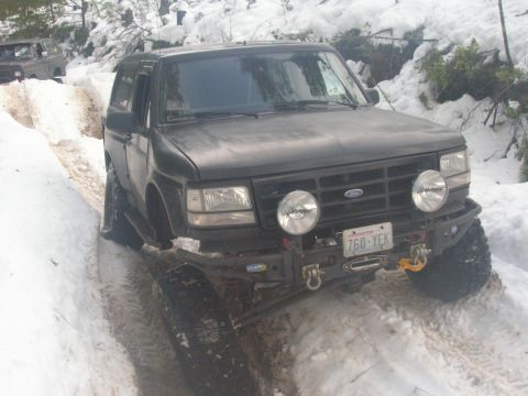 1996 Ford Bronco - A black Ford Bronco navigates a snow-covered path, with another vehicle visible in the background.
