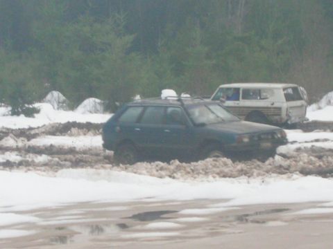 1996 Ford Bronco - Two vehicles are stuck in a muddy, snow-covered area with trees in the background.