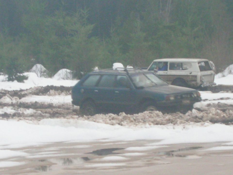Dark station wagon stuck in mud and snow, with a white van behind it