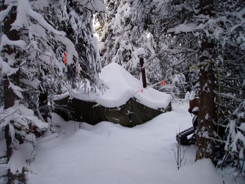 2000 Ford E350 - A tent covered in snow with a stovepipe protruding, situated in a dense, snow-laden forest.