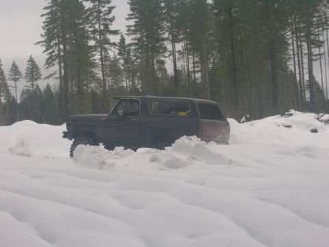 1996 Ford Bronco - This dark SUV navigates through a snowy landscape, its tires kicking up snow as it drives.