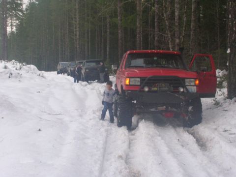1996 Ford Bronco - Several off-road vehicles drive through a snowy forest trail.