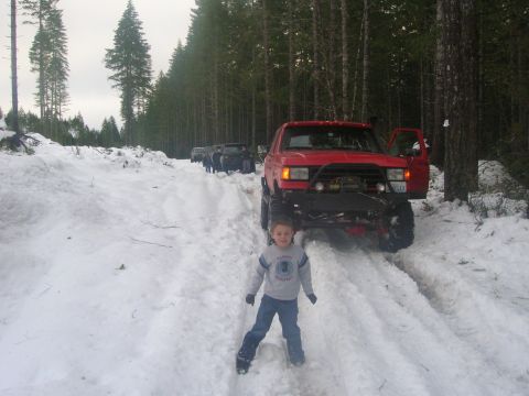 1996 Ford Bronco - A group of off-road vehicles navigate a snow-covered path through a forest.
