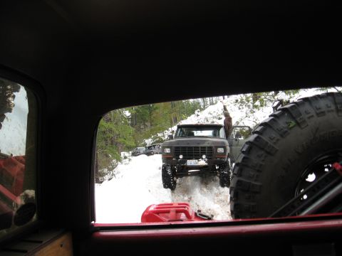 1989 Ford Bronco - A convoy of off-road vehicles navigates a snowy trail, with one Bronco stopped to allow a passenger to exit.