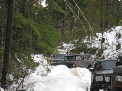 1989 Ford Bronco - Several SUVs, including a 1989 Ford Bronco, navigate a snowy trail in a wooded area.
