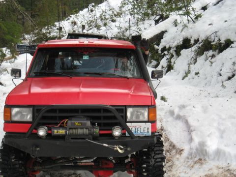 1989 Ford Bronco - Red 1989 Ford Bronco navigating a snowy off-road trail with another vehicle visible behind.
