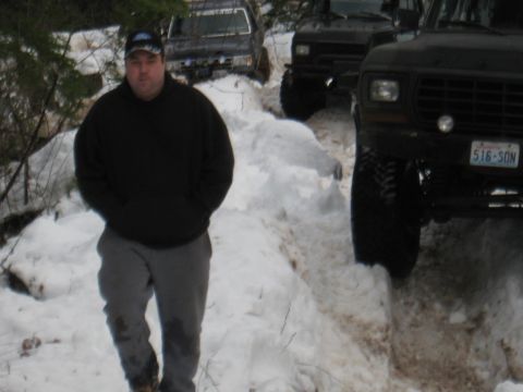 1989 Ford Bronco - Man walks in snow with multiple off-road vehicles on a trail.