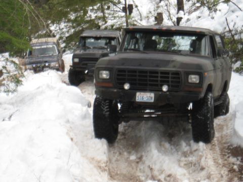 1989 Ford Bronco - Several modified SUVs navigate a snowy trail, with the lead vehicle displaying a license plate.