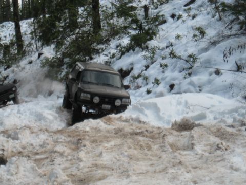 1989 Ford Bronco - An SUV navigates a snowy, wooded terrain, with another vehicle visible in the background.