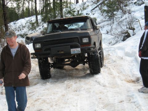 1989 Ford Bronco - A lifted black Ford Bronco navigates a snowy trail, with another vehicle visible in the background.