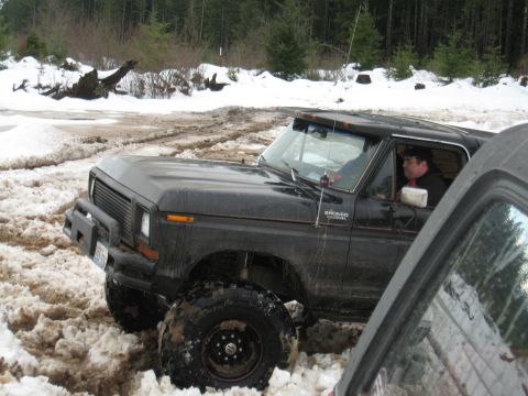 1989 Ford Bronco - Black 1989 Ford Bronco navigates a snowy and muddy trail with a driver inside.