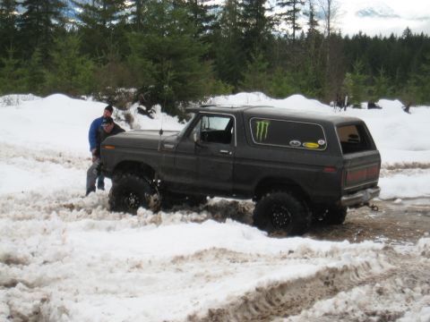 1989 Ford Bronco - A dark brown Ford Bronco is stuck in the snow with two people attempting to free it.