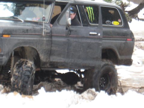 1989 Ford Bronco - A driver navigates a muddy, snow-covered terrain in a lifted off-road vehicle.
