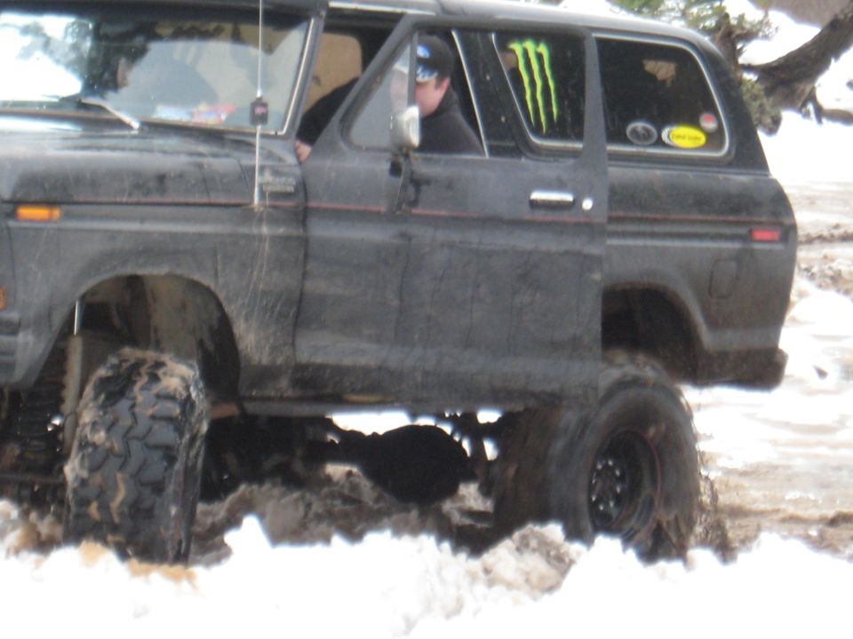 Muddy off-road vehicle with door open, driving through snow. Monster Energy sticker on rear window
