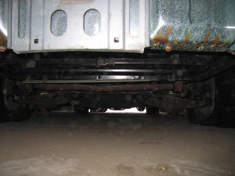 1991 Ford LTD Crown Victoria - The undercarriage of a vehicle is visible, with suspension and exhaust systems apparent. Rust is present on the upper bodywork.