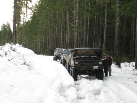 1989 Ford Bronco - Several off-road vehicles parked on a snow-covered forest road, with hoods open on the lead vehicle.