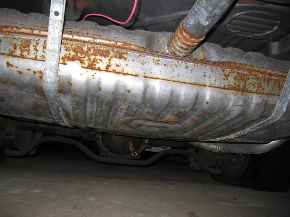Undercarriage view of a rusty fuel tank and exhaust system