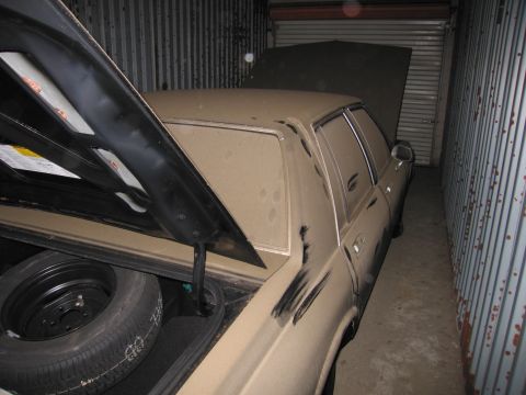 1991 Ford LTD Crown Victoria - A dusty sedan sits in a storage unit with its trunk and hood open, revealing a spare tire.