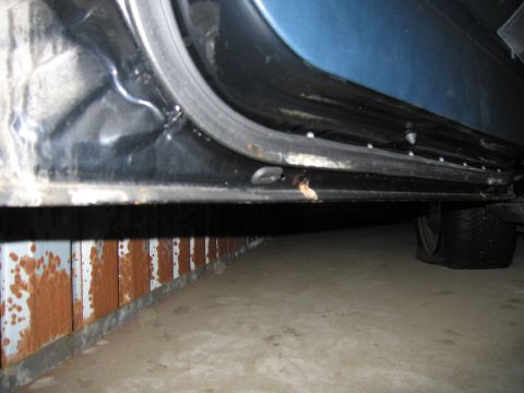 1991 Ford LTD Crown Victoria - Close-up of a car's lower door frame reveals rust and damage, with a flat tire visible.