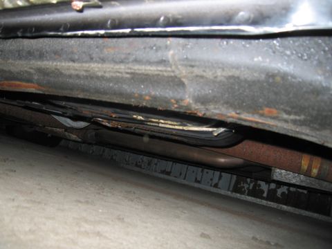 1991 Ford LTD Crown Victoria - The underside of a vehicle reveals significant rust on the rocker panel and exhaust components.