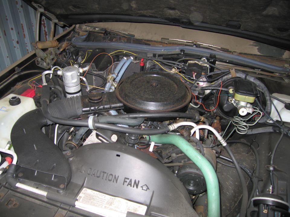 Engine bay with air cleaner, hoses, and master cylinder visible. "CAUTION FAN" text on shroud